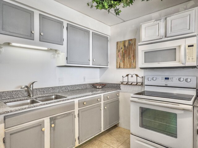 kitchen featuring white appliances, light tile patterned floors, gray cabinets, and a sink