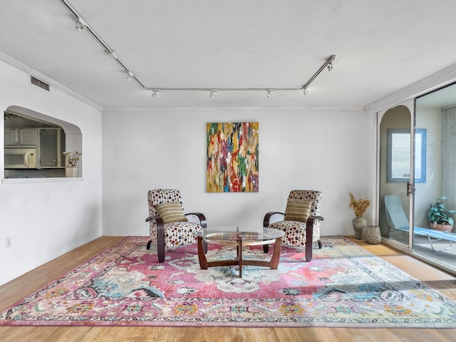 living area with visible vents, arched walkways, wood finished floors, and ornamental molding