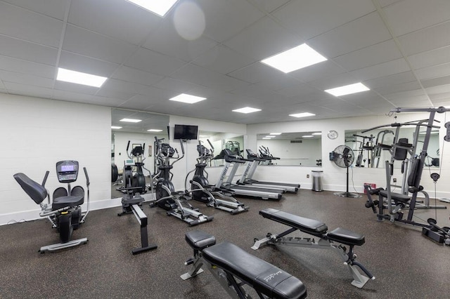 exercise room featuring a paneled ceiling and baseboards