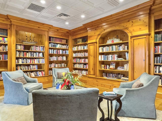 sitting room featuring bookshelves, an ornate ceiling, visible vents, and wooden walls