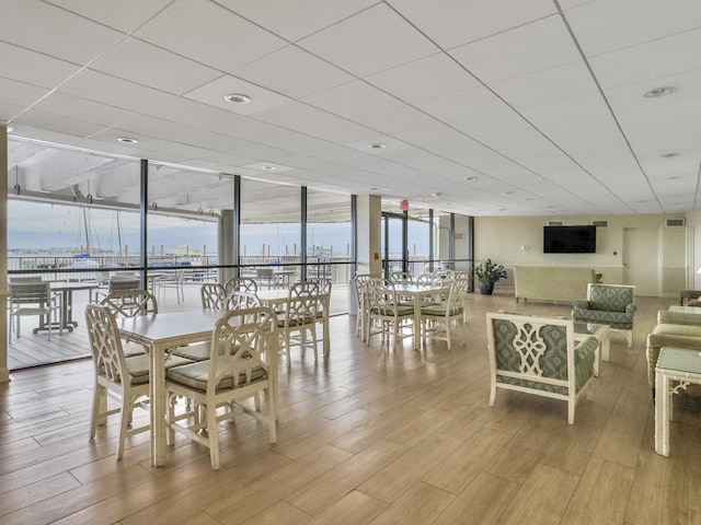 dining room featuring a drop ceiling, a wall of windows, and wood finished floors