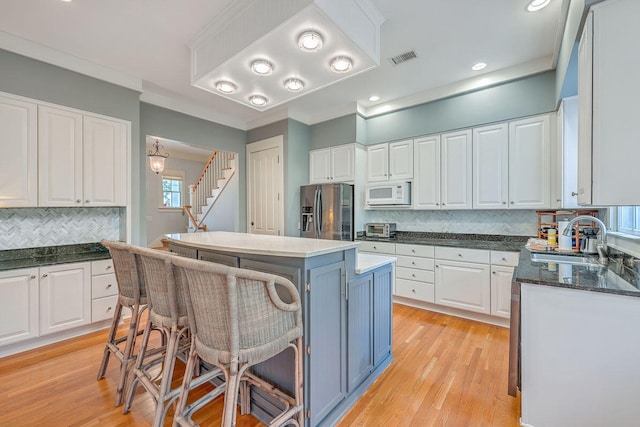 kitchen featuring stainless steel fridge, tasteful backsplash, white microwave, a center island, and white cabinetry