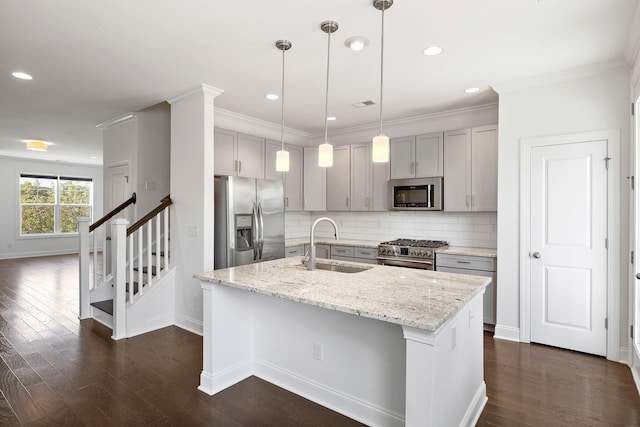 kitchen with sink, hanging light fixtures, a kitchen island with sink, light stone counters, and stainless steel appliances