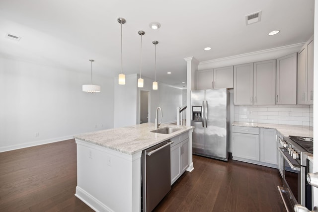 kitchen featuring pendant lighting, sink, stainless steel appliances, light stone countertops, and an island with sink