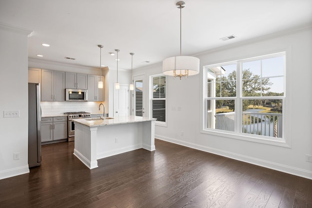 kitchen featuring appliances with stainless steel finishes, pendant lighting, an island with sink, gray cabinetry, and light stone counters