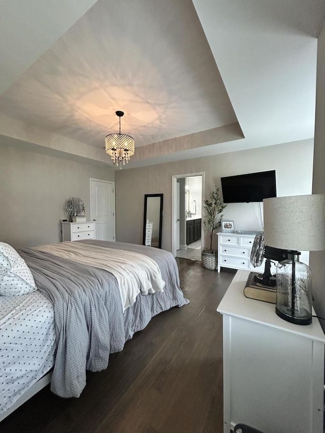 bedroom featuring a chandelier, dark wood-style floors, a raised ceiling, ensuite bath, and baseboards