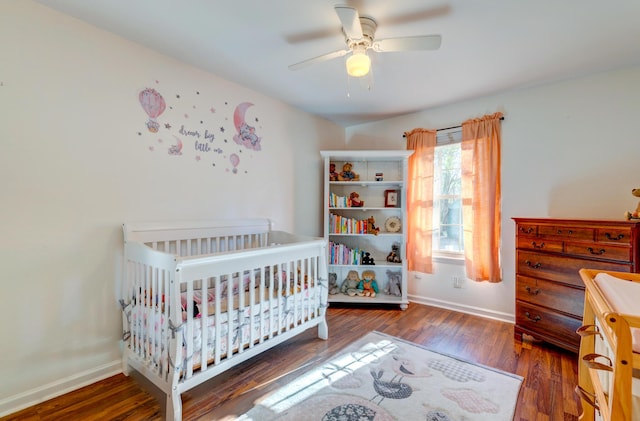 bedroom featuring a nursery area, ceiling fan, and dark hardwood / wood-style floors