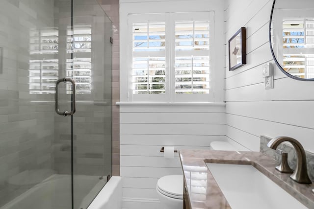 full bathroom featuring enclosed tub / shower combo, vanity, wooden walls, and toilet