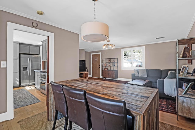 kitchen featuring crown molding, stainless steel appliances, decorative light fixtures, and light hardwood / wood-style floors