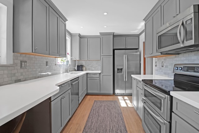 kitchen with stainless steel appliances, light hardwood / wood-style floors, sink, and gray cabinetry