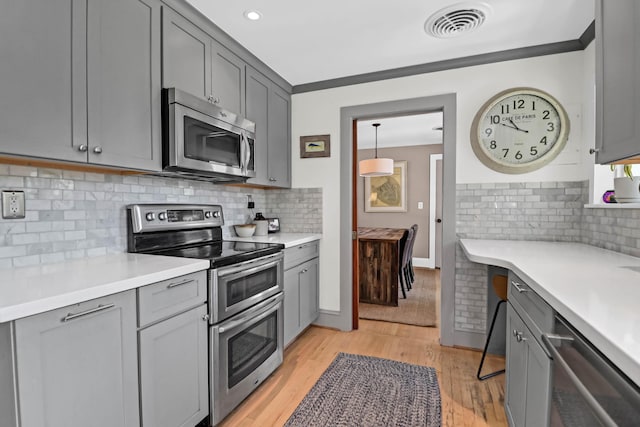 kitchen with gray cabinets, backsplash, light hardwood / wood-style floors, stainless steel appliances, and crown molding