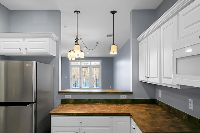 kitchen with hanging light fixtures, white cabinetry, and stainless steel refrigerator