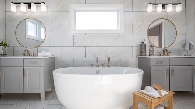 full bath featuring marble finish floor, two vanities, a freestanding bath, and a sink