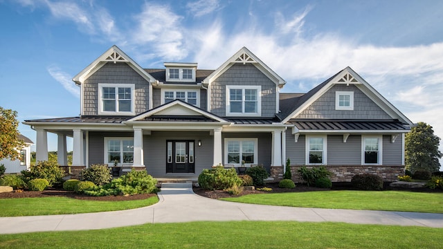 craftsman inspired home with metal roof, covered porch, stone siding, a standing seam roof, and a front yard