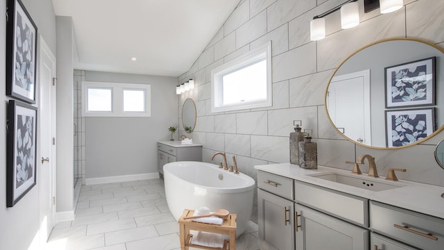 bathroom featuring lofted ceiling, two vanities, a sink, tile walls, and a soaking tub