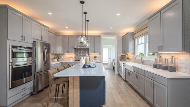 kitchen with light countertops, appliances with stainless steel finishes, gray cabinets, and a kitchen breakfast bar