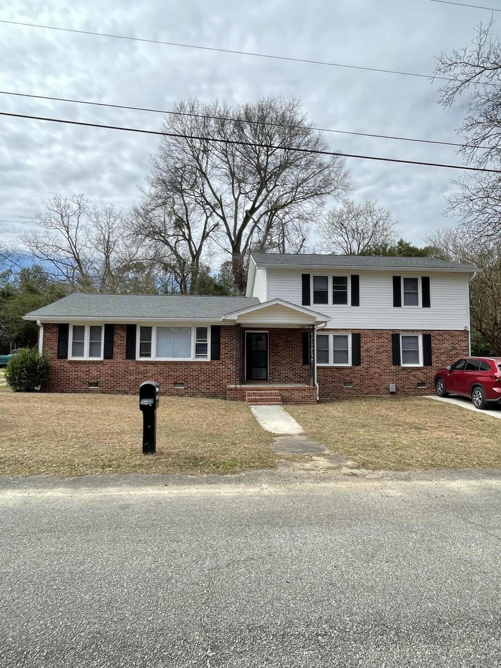 view of front of home with crawl space, brick siding, a front lawn, and roof with shingles