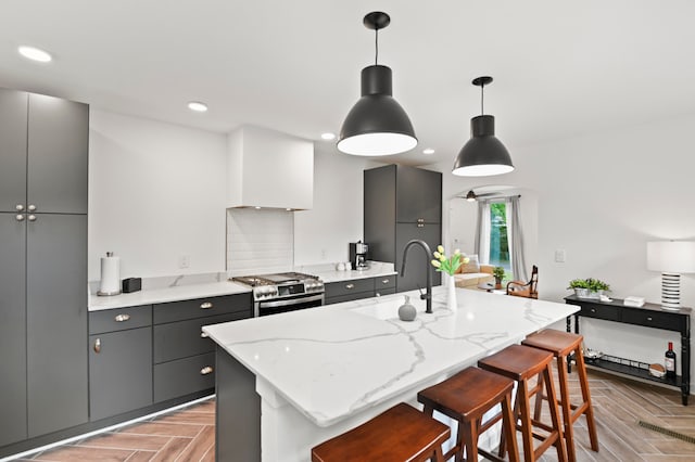 kitchen featuring sink, stainless steel gas range, pendant lighting, a kitchen bar, and a center island with sink