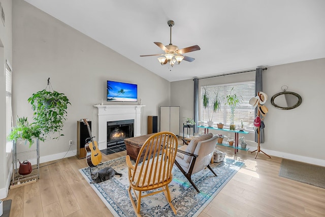 living room with a ceiling fan, vaulted ceiling, a fireplace with flush hearth, and light wood-style floors
