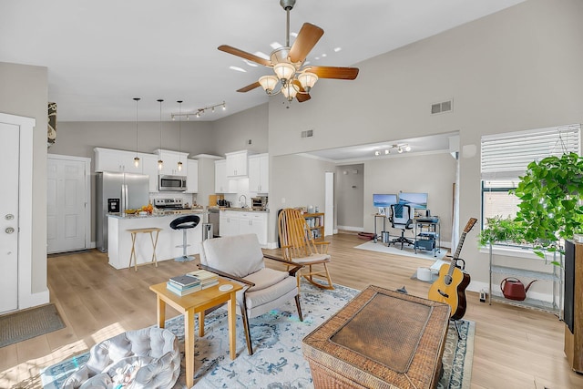 living area with high vaulted ceiling, a ceiling fan, light wood-style flooring, and visible vents