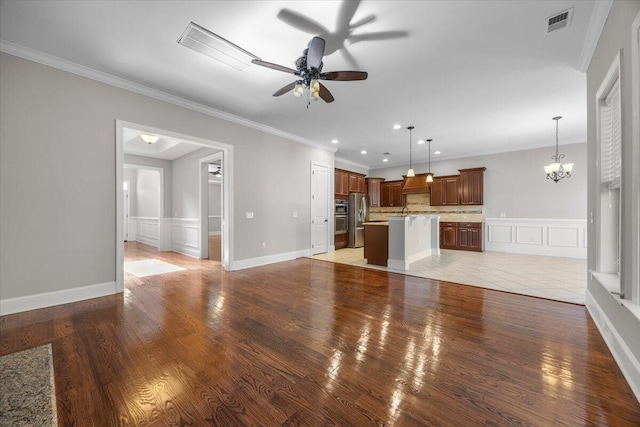 unfurnished living room featuring light wood finished floors, visible vents, ornamental molding, a decorative wall, and ceiling fan with notable chandelier