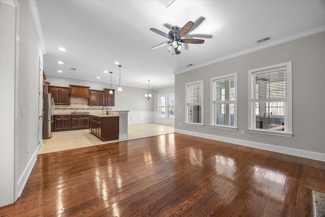 unfurnished living room featuring ornamental molding, light wood-type flooring, a sink, and visible vents