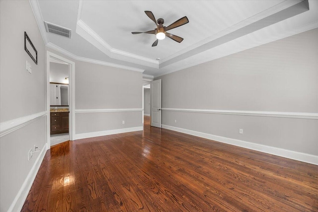 spare room with visible vents, a ceiling fan, dark wood-style floors, ornamental molding, and a tray ceiling