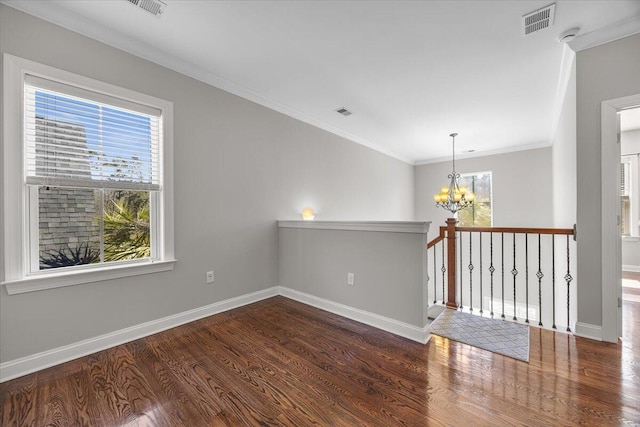 empty room with dark wood finished floors, visible vents, ornamental molding, a chandelier, and baseboards