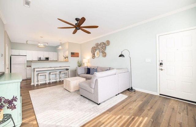 living area featuring wood finished floors, ceiling fan, baseboards, ornamental molding, and visible vents