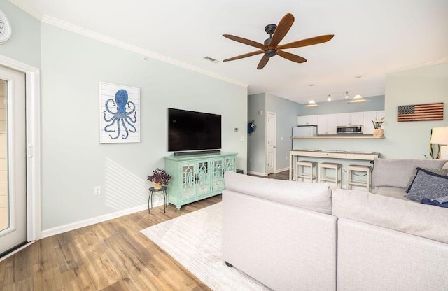 living area featuring wood finished floors, visible vents, crown molding, baseboards, and ceiling fan