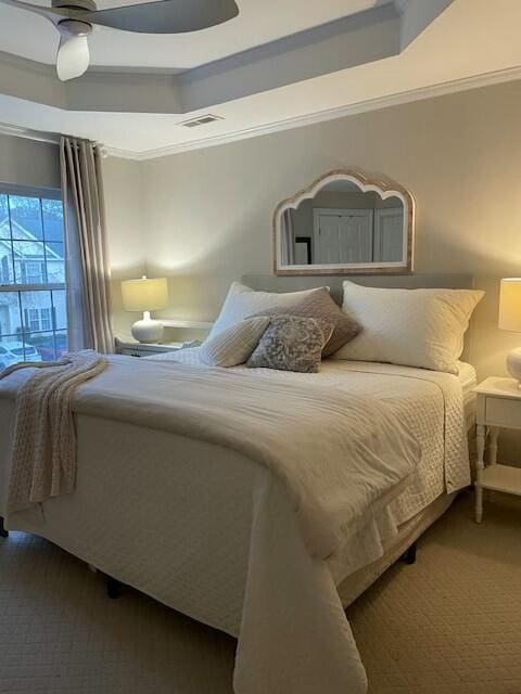 bedroom featuring carpet floors, a tray ceiling, crown molding, visible vents, and a ceiling fan