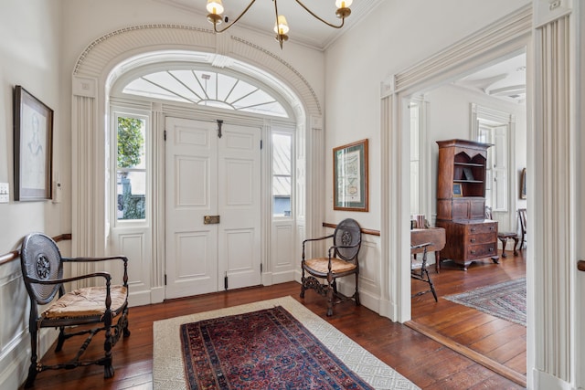 entryway featuring an inviting chandelier, ornamental molding, dark wood-type flooring, and a wainscoted wall