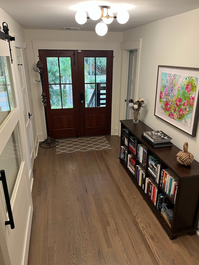 doorway featuring visible vents, a chandelier, a barn door, french doors, and wood finished floors