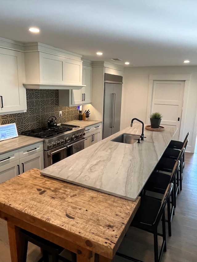 kitchen featuring a kitchen bar, high quality appliances, a center island with sink, a sink, and light stone counters