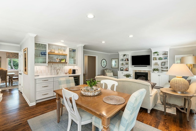 dining room featuring dark wood-type flooring, a tiled fireplace, indoor wet bar, and recessed lighting