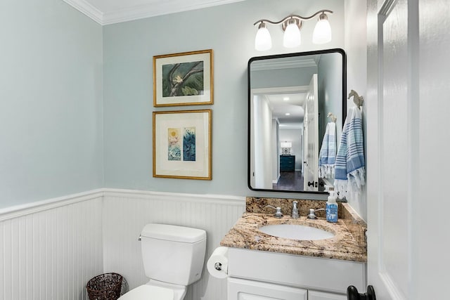 bathroom featuring vanity, toilet, ornamental molding, and a wainscoted wall