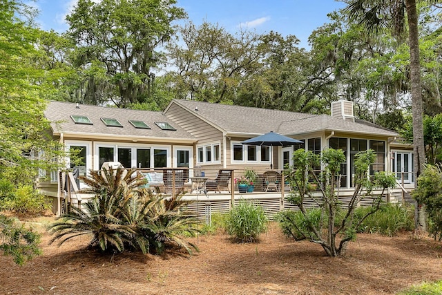 rear view of house with a wooden deck, a sunroom, a shingled roof, and a chimney