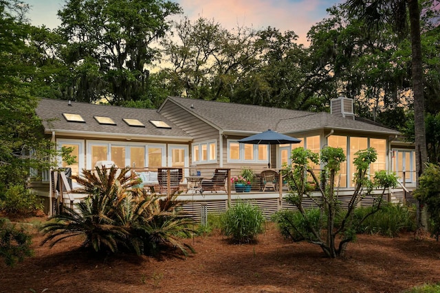 rear view of house with a wooden deck, a shingled roof, a chimney, and a sunroom
