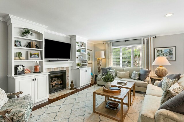 living area with a tile fireplace, crown molding, built in shelves, and wood finished floors