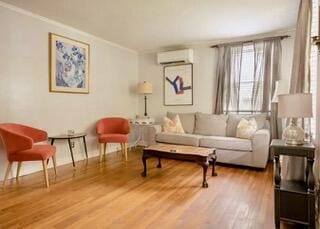 living area featuring hardwood / wood-style floors, a wall unit AC, and crown molding