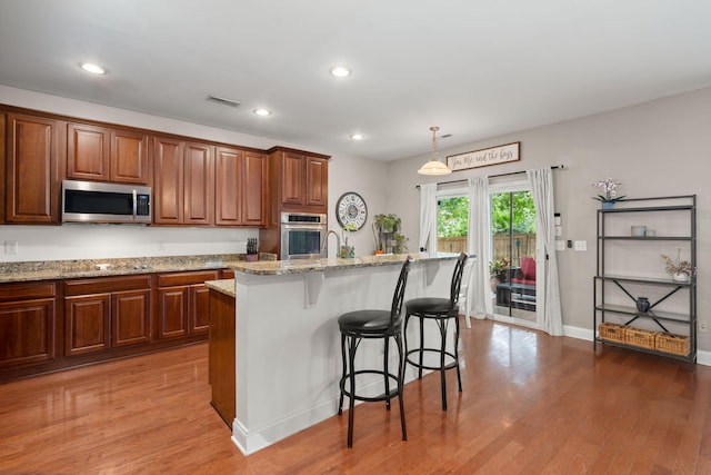 7030 Billberry St, Hanahan, SC 29410 - kitchen with appliances with stainless steel finishes, light stone counters, wood finished floors, a breakfast bar, and recessed lighting