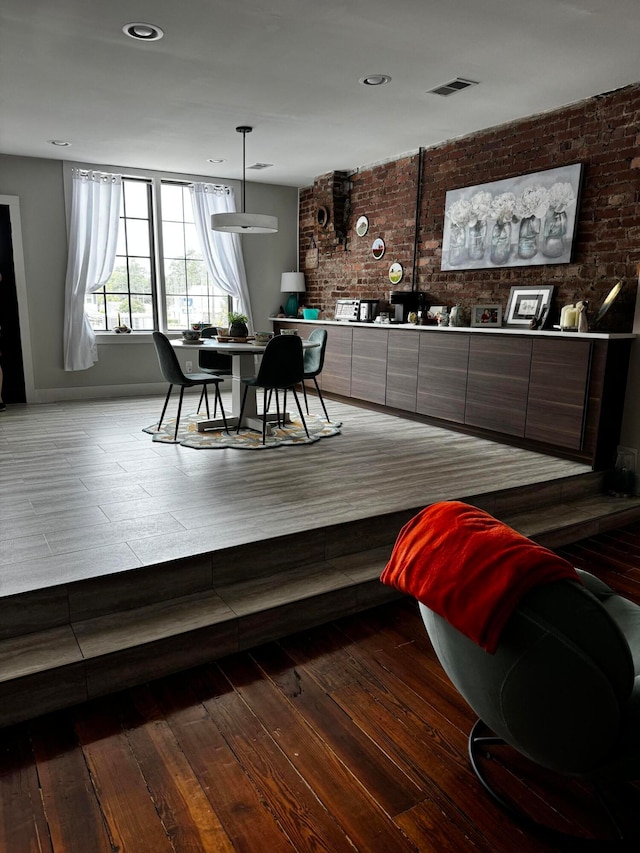 dining area with wood-type flooring and brick wall