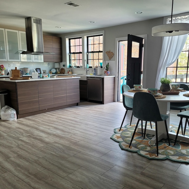 kitchen with light countertops, visible vents, island exhaust hood, modern cabinets, and stainless steel dishwasher