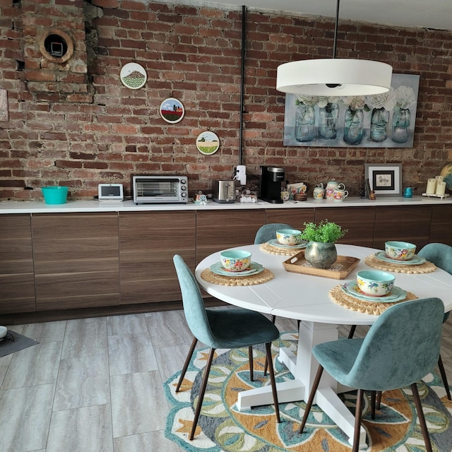 dining space featuring light wood-style floors, brick wall, and a toaster