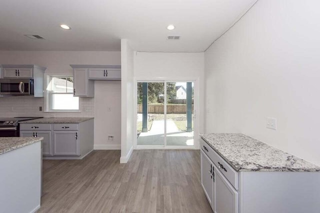 kitchen featuring light stone countertops, appliances with stainless steel finishes, tasteful backsplash, gray cabinets, and light hardwood / wood-style floors