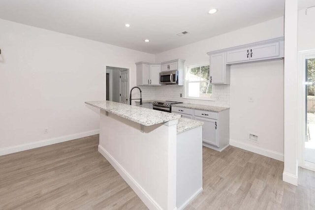 kitchen with sink, stainless steel appliances, light stone counters, light hardwood / wood-style flooring, and an island with sink