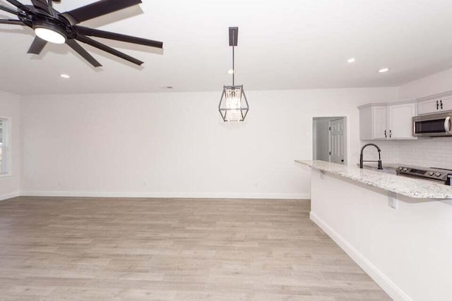 kitchen featuring white cabinets, a kitchen breakfast bar, appliances with stainless steel finishes, decorative light fixtures, and light stone counters