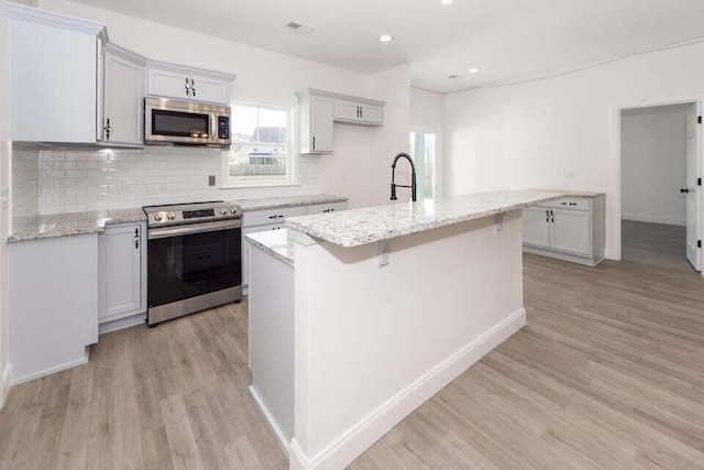 kitchen featuring light stone counters, stainless steel appliances, a kitchen island with sink, sink, and light hardwood / wood-style flooring