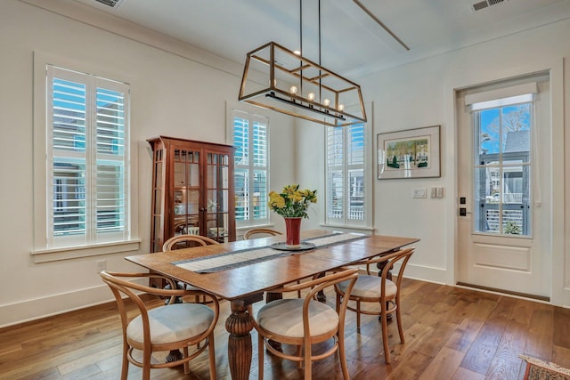 dining space featuring visible vents, crown molding, baseboards, a notable chandelier, and wood-type flooring