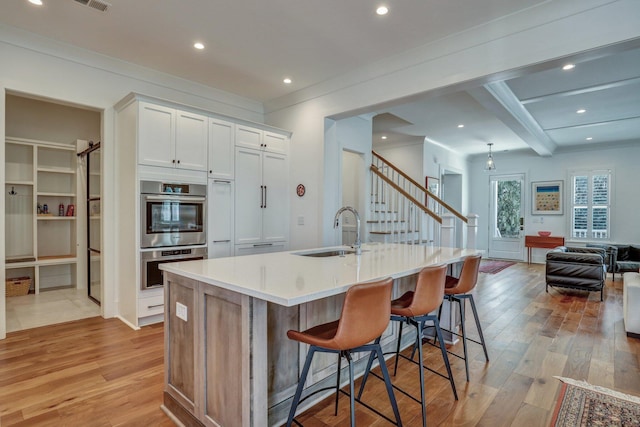 kitchen with light wood finished floors, stainless steel double oven, white cabinetry, and a sink